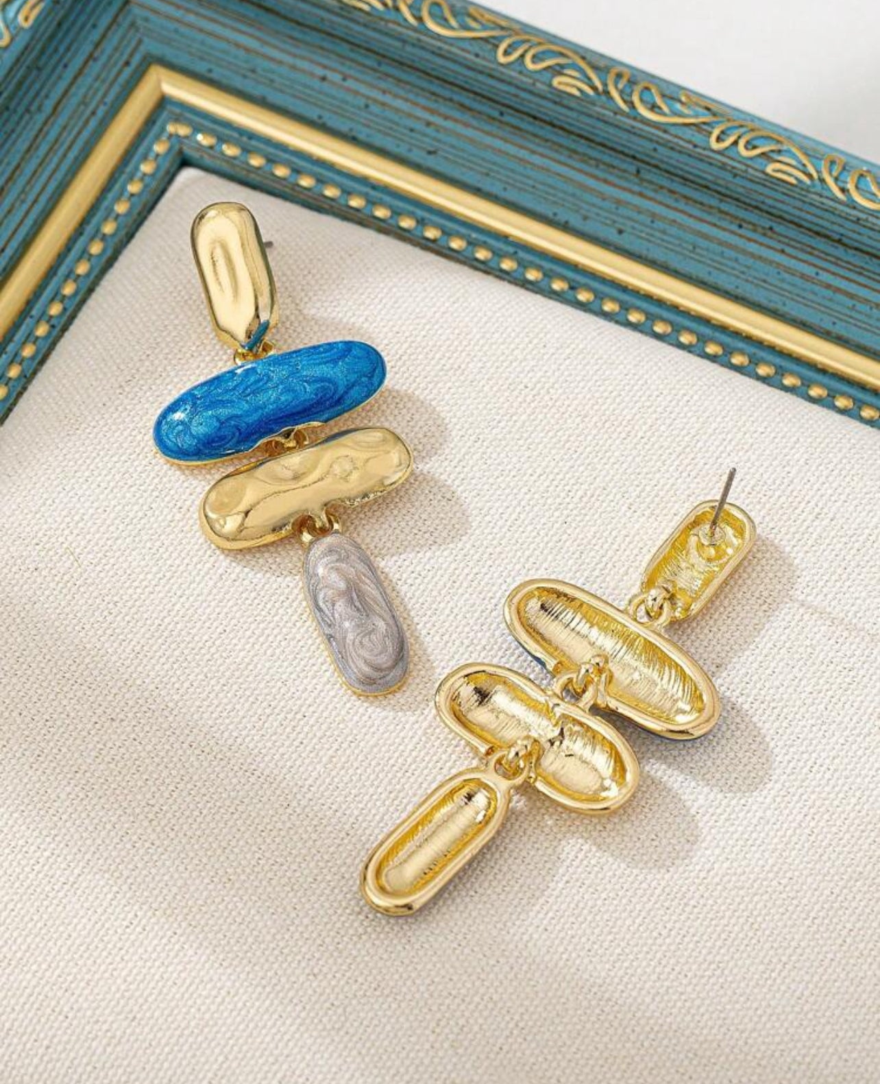 Unikt designade asymmetriska örhängen i blå nyanser med detaljer i guld och silver.